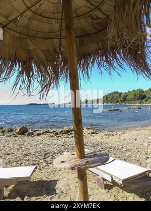 Sandy beach beach with sun loungers under a thatched roof, directly on the calm blue sea, katakolon, mediterranean sea, greece Stock Photo