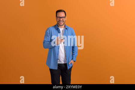 Male professional laughing and checking social media apps over mobile phone on orange background Stock Photo
