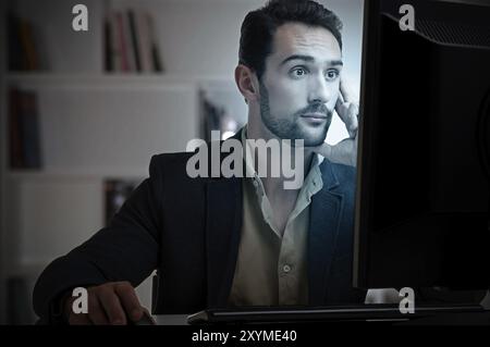 Surprised man looking at a computer screen, in a dark room Stock Photo