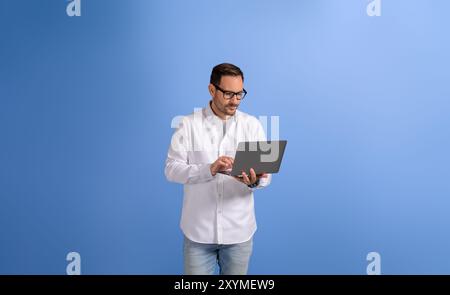 Serious handsome businessman checking e-mails over wireless computer and standing on blue background Stock Photo