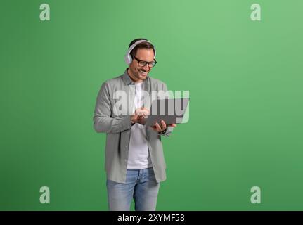 Young businessman wearing headphones and discussing over video call on laptop over green background Stock Photo