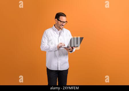 Portrait of smiling confident businessman doing online research over laptop on orange background Stock Photo