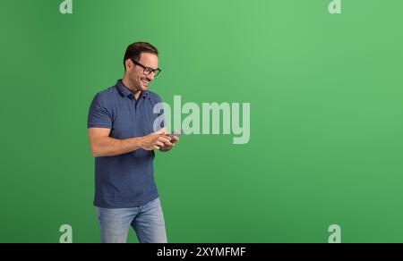 Portrait of confident young man smiling and checking e-mails over smart phone on green background Stock Photo