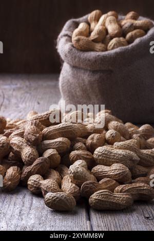 Peanuts in a burlap sack on wooden background Stock Photo