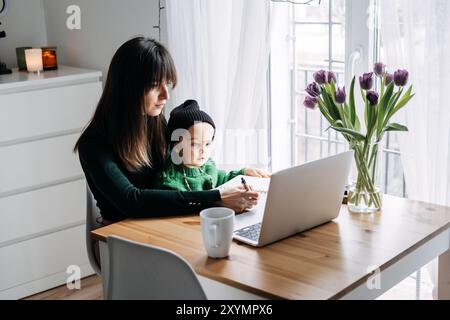 Mother working from home with toddler on lap. Remote work, parenting challenges, work-life balance, family time, flexible work arrangements Stock Photo