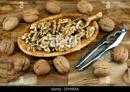 walnut (Juglans regia), cracked walnuts on a wooden plate with whole nuts, wooden scoop and nutcracker Stock Photo