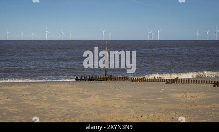 North sea coast in Caister-on-Sea, Norfolk, England, UK, with a wave breaker and wind turbines in the background Stock Photo