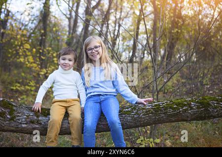 Kids play in autumn park. Little brother and his sister sitting on the tree in the fall Stock Photo