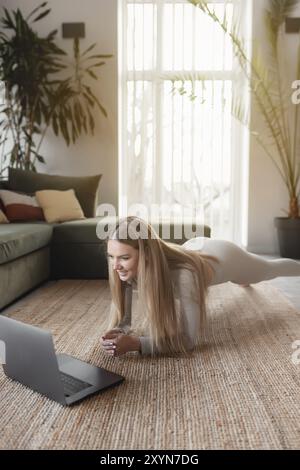 Healthy sport lifestyle concept, happy smiling blogger girl doing yoga exercises at home with green loft interior watching and repeating trainer exerc Stock Photo