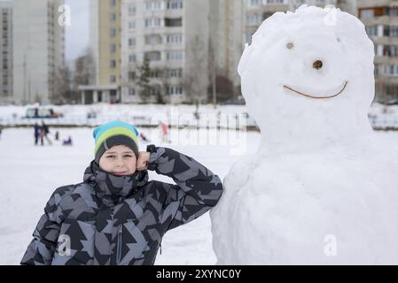 Teen boy standing near a big snowman Stock Photo