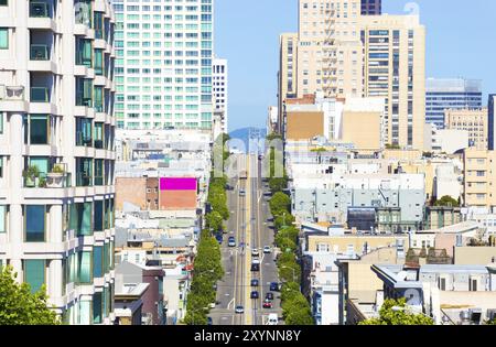 Distant telephoto view down California Street of iconic cable car and tip of Bay Bridge among residential apartment buildings on clear sunny day in Sa Stock Photo