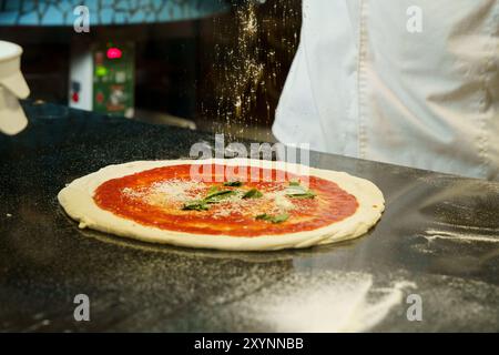 A chef preparing a pizza with tomato sauce and parmesan cheese Stock Photo