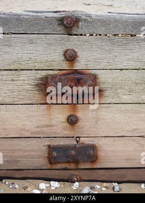 close up detail of a rusty rusting metal nuts bolts washers fittings on timber wood groyne lines with sandy beach in background and foreground Stock Photo