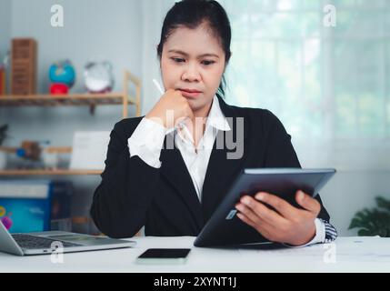 Businesswoman in black suit using digital tablet and working on laptop computer on table at office. Businesswoman finger touching on tablet screen at Stock Photo