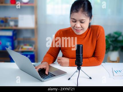 Woman talking into microphone on stand, lead on-line communication, discuss topic, looks at notebook screen, engaged in streaming, virtual meeting eve Stock Photo