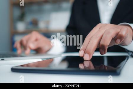 Businesswoman in black suit using digital tablet and working on laptop computer on table at office. Businesswoman finger touching on tablet screen at Stock Photo