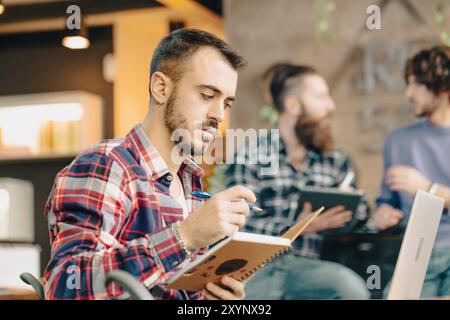 Young man is taking notes in a notebook during a meeting with colleagues Stock Photo
