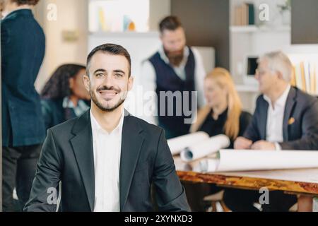 Young businessman is smiling while his colleagues are working in the background Stock Photo