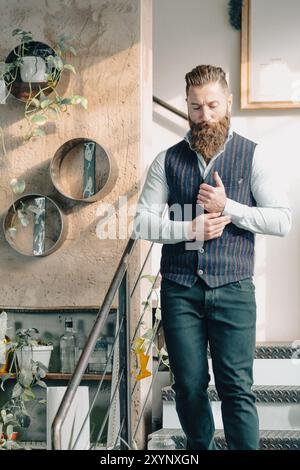 Bearded businessman with a shaved head and wearing a vest adjusting his shirt while walking down stairs in an office Stock Photo