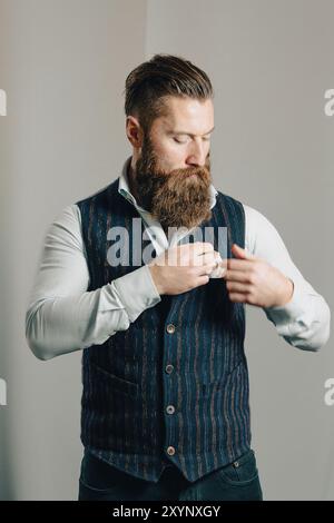Casually dressed businessman with a beard is buttoning his waistcoat while getting ready for work Stock Photo