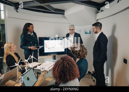 Diverse team of businesspeople is discussing in a meeting about renewable energies, analyzing data and planning future investments Stock Photo