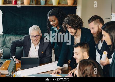 Diverse team of architects and designers are collaborating on a project, using a digital tablet and blueprints spread out on a table Stock Photo
