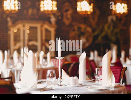 White candles in candlestick stylish glasses and folded napkins on plates in modern restaurant Stock Photo