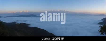 Panoramic view of distant Himalayan mountain peaks glowing red from morning sunrise light above an undulating sea of clouds seen from Bandipur, Nepal, Stock Photo