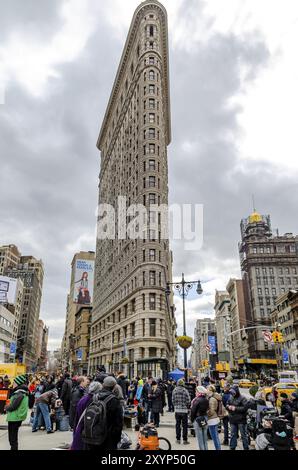 Flatiron Building New York City with lots of People standing in the forefront low angle view during daylight, overcast, vertical Stock Photo