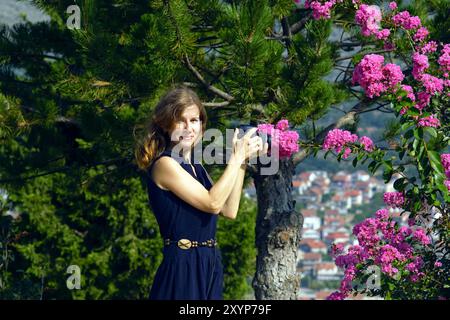 Attractive smiling woman taking photo with professional camera near trees and flowers. Portrait of female photographer taking photoshoot outdoors Stock Photo