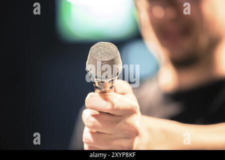 Young man on the stage is talking into a microphone, speech, face is blurry Stock Photo