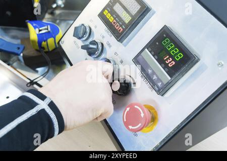 A close-up of a man's hand holds a rotary switch on the equipment control panel with instruments Stock Photo