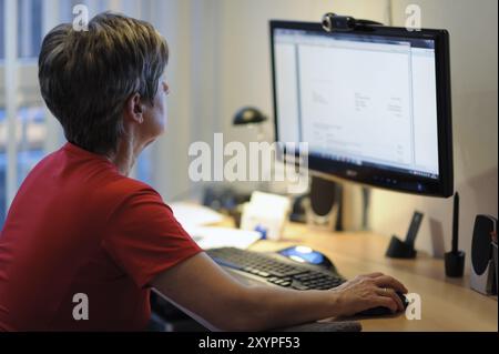 A woman sits at a desk and works on a PC Stock Photo