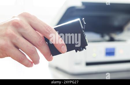 Third party printer cartridge in the hand, printer in the blurry background Stock Photo