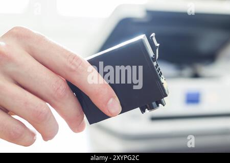 Third party printer cartridge in the hand, printer in the blurry background Stock Photo