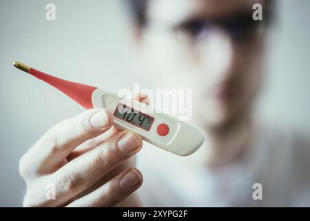 Man holds a red fever thermometer with high temperature in his hand, blurry face Stock Photo