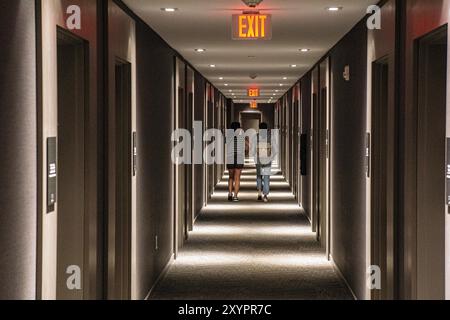 Rear view of two people walking down hotel hallway, diminishing perspective Stock Photo