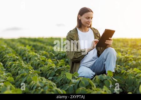 Female farmer uses digital tablet for analyse and check soybeans plants at field. Modern agribusiness. Agronomist controls growth and development of s Stock Photo