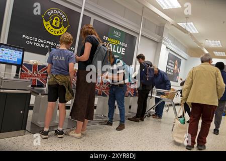 Marks and Spencer supermarket inside interior people paying for food at self-service checkout with Union Jack paper shopping bags Oxford UK 2024 Stock Photo