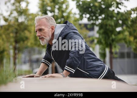 Mature fit man doing push ups on bench working out regularly in city park, copy space Stock Photo