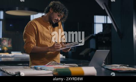 Indian business man arabian businessman decorator male tailor fashion designer couturier multitasking work talking mobile phone with client writing Stock Photo