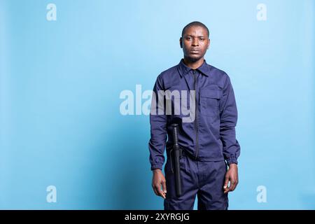 Portrait of african american security officer posing in studio, wearing a patrolling service uniform equipped with a baton for his own protection. Guard on duty shows his authority. Stock Photo