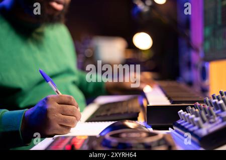 Songwriter taking notes to create new tracks for an album in his home studio, writing lyrics and harmonic elements before recording his song and editing on software, acoustical engineering. Stock Photo