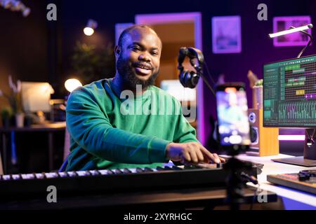 Musician doing online paid classes to help people play piano notes, teaching lessons from his home studio and recording video tutorials. Musical instructor playing midi controller keyboard. Stock Photo