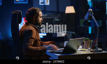 Technician typing code in neon lit personal office, using javascript programming language to develop software application. It specialist using multimonitor desktop setup to finish project, camera A Stock Photo