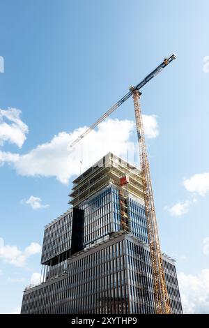 Construction site of modern glass facade skyscraper building with a crane against clear sky background, constructing Sickla Central office building Stock Photo