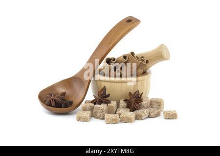 Star anise in a wooden spoon, wooden mortar filled with cinnamon sticks and brown sugar cubes isolated on white background Stock Photo