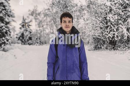 Young adult man with brown short hair standing at beautiful snow landscape during winter in norway, wearing a blue rain jacket, looking at camera, nor Stock Photo