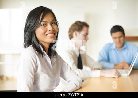 An attractive Asian businesswoman looks at the camera during a meeting with a diverse group of business people including a latino and caucasian male Stock Photo
