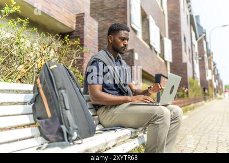 Side view portrait of a young african man working with laptop sitting on a city bench Stock Photo